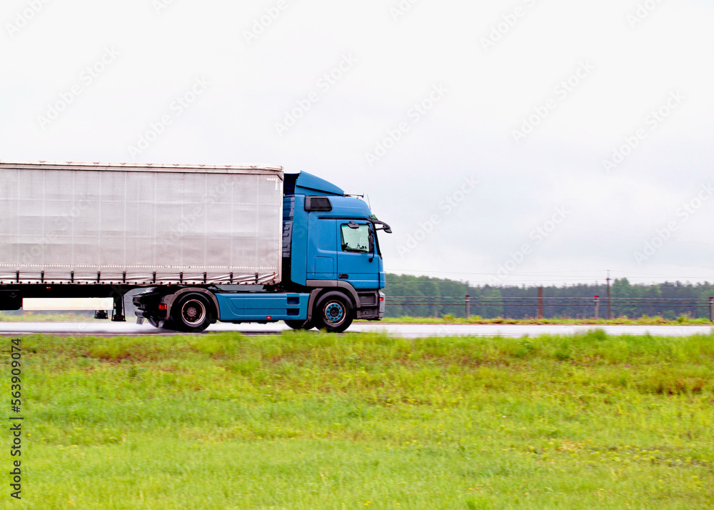 A truck with a semi-trailer transports cargo in rainy weather on a slippery road. Automobile cargo transportation. Copy space for text