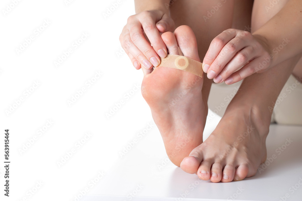 Woman sticks a medical plaster to the plantar wart of the leg to remove dead skin and calluses. Copy space for text Woman sticks a medical plaster to the plantar wart of the leg to remove dead skin and calluses. Copy space for text