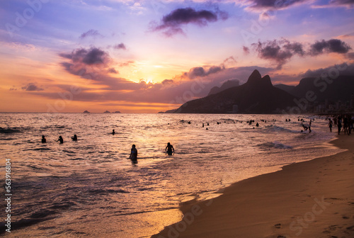 Silhouettes of beachgoers in Rio de Janeiro, Brazil playing on the sand and in the water of the Atlantic Ocean as the sun sets over the sea near Ipanema Beach.