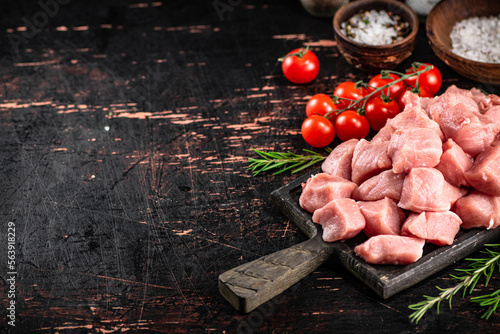 Pieces of raw pork on a cutting board with spices, tomatoes and rosemary. 
