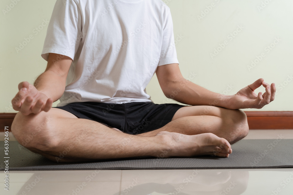 Healthy man on white t-shirt is yoga meditating alone at indoor home. Man doing meditation, yoga practicing in lotus pose for relax, relief stress, serenity. Meditation yoga is wellness mind exercise.