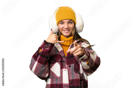 Teenager caucasian girl wearing winter muffs over isolated background making phone gesture and pointing front