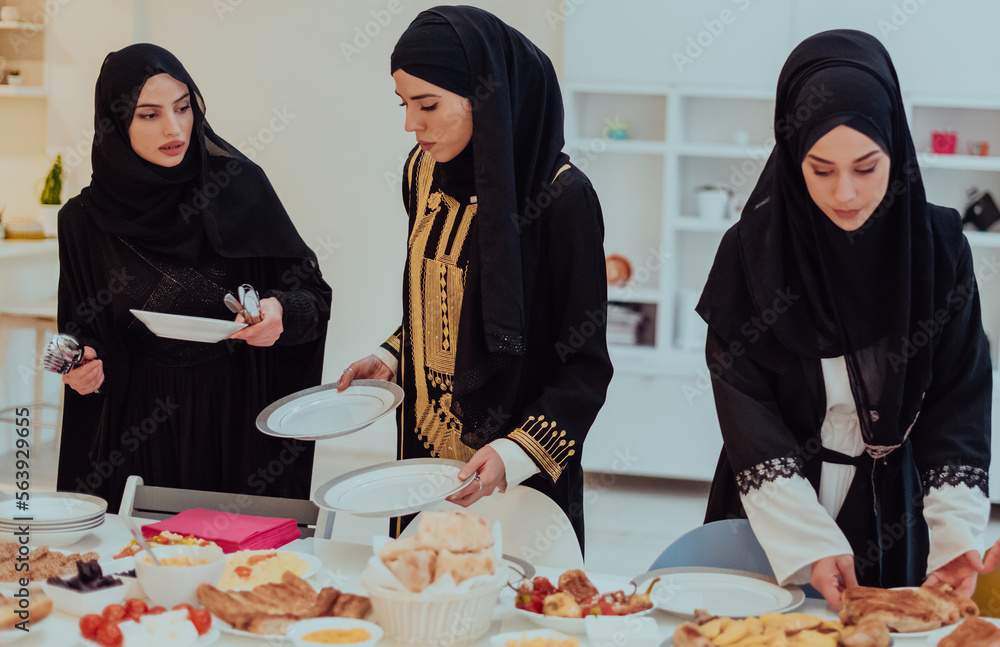 Eid Mubarak Muslim family having Iftar dinner young muslim girls serving food on the table during Ramadan feasting month at home. The Islamic Halal Eating and Drinking Islamic family Eid Mubarak Muslim family having Iftar dinner young muslim girls serving food on the table during Ramadan feasting month at home. The Islamic Halal Eating and Drinking Islamic family