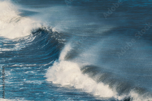 Blue ocean wave with splashing hitting on black sand beach in summer