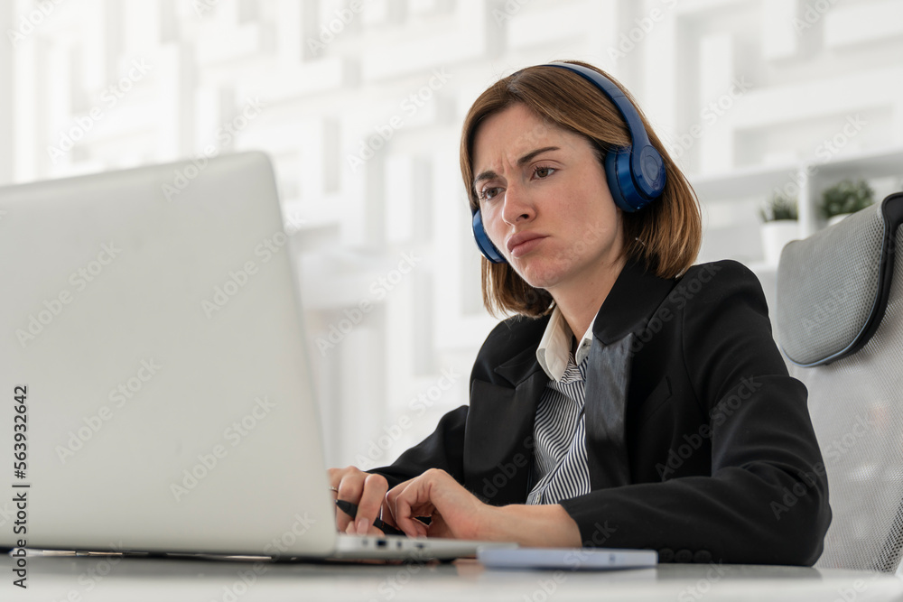 Portrait of successful and attractive business woman in headphones listening to music in her office. Positive female employee in black suit smiling and sitting at the desk in her modern workplace Portrait of successful and attractive business woman in headphones listening to music in her office. Positive female employee in black suit smiling and sitting at the desk in her modern workplace