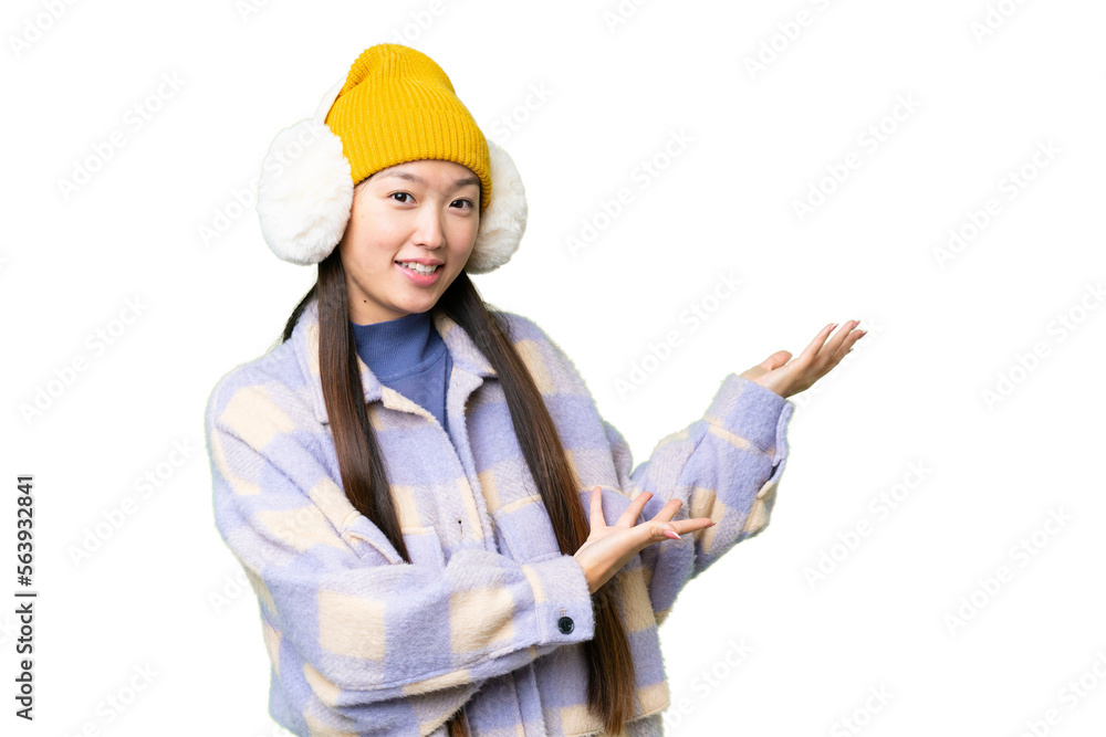 Young Asian woman wearing winter muffs over isolated chroma key background extending hands to the side for inviting to come Young Asian woman wearing winter muffs over isolated chroma key background extending hands to the side for inviting to come