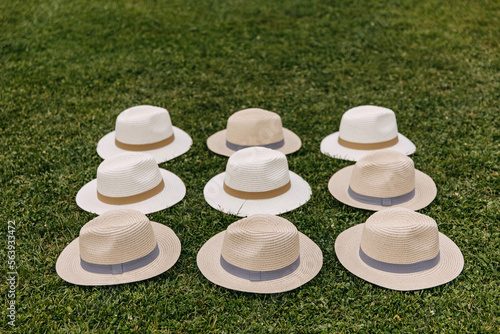 Nine white and beige summer hats placed on green grass.