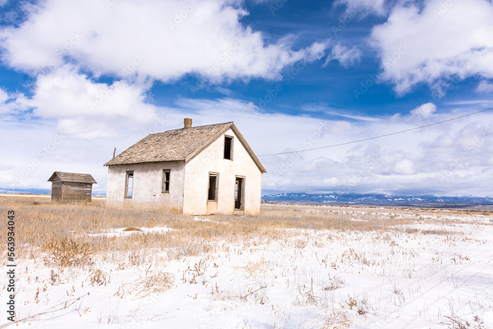Abandoned homestead with out building on potato farm, San Luis Valley, Colorado, with blue sky, clouds, and snow on a winter day