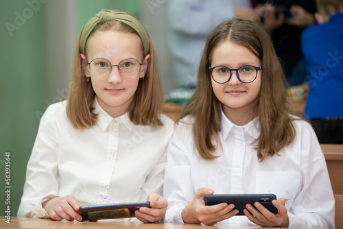 Schoolgirls sit at their desks and hold smartphones in their hands.