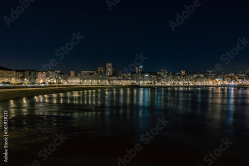 The city is illuminated at night. Embankment near the sea, the rays are reflected in the water.