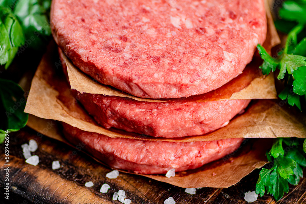 Raw burger on a cutting board with parsley and salt. Raw burger on a cutting board with parsley and salt.
