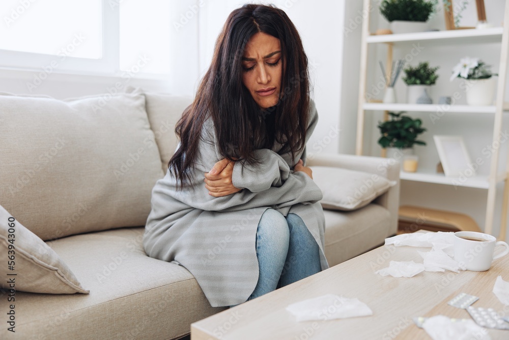 A woman with a cold pills is treated at home chooses which medicines to take and self-medicates, checks the expiration date while sitting at home on the couch, temperature, allergies and covid-19