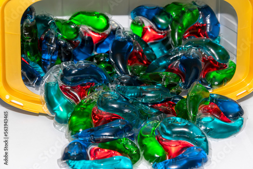 multi-colored capsules for washing clothes rashing from a plastic container on a white background