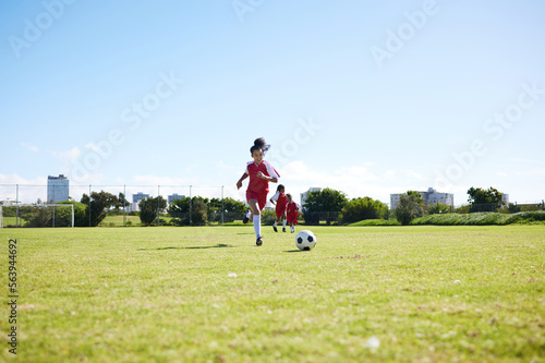 Soccer, training or children and a girl team playing with a ball together on a field for practice. Fitness, football and grass with kids running or dribblinf on a pitch for competition or exercise