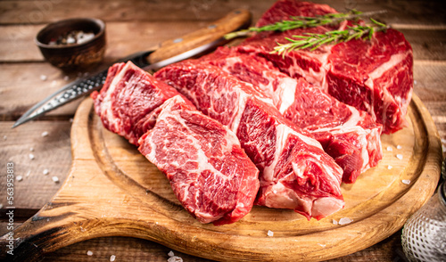 Raw beef on a cutting board with rosemary and spices. 