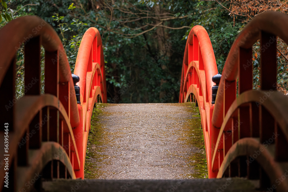 Red railings on empty arched bridge with trees and foliage in background Red railings on empty arched bridge with trees and foliage in background
