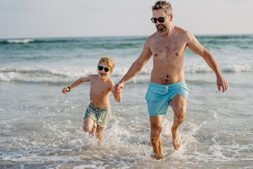 Father with his little son running out of the ocean, enjoying summer vacation.