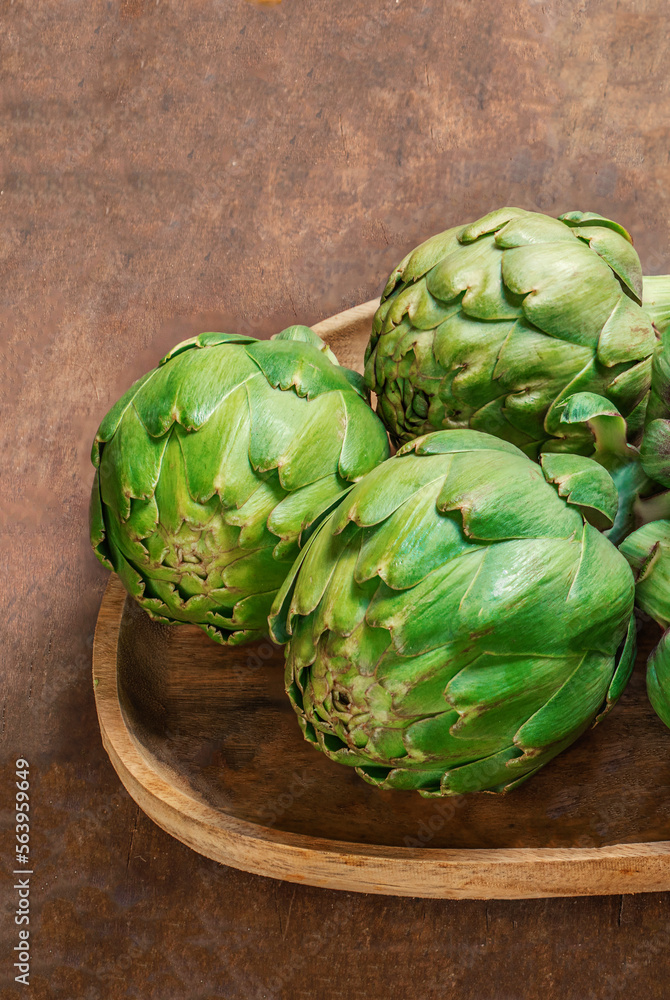 Fototapeta premium Artichoke flower buds. Fresh and raw artichoke on the wooden table. Copyspace. Top view.