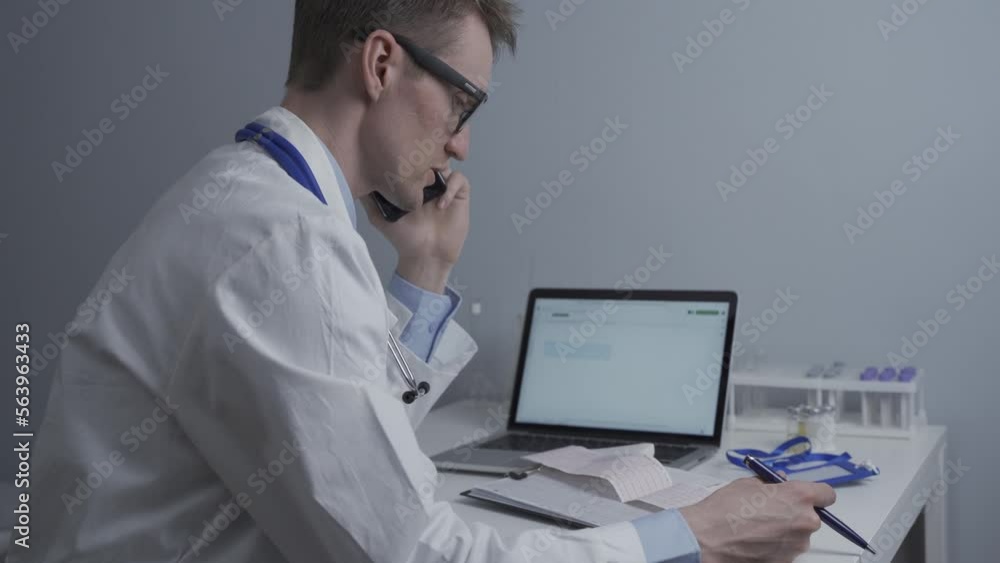 Doctor cardiologist examining electrocardiogram of patient's heart and consults him by phone in office of clinic at table near computer. Healthcare and medicine. Diagnosis and treatment of disease.