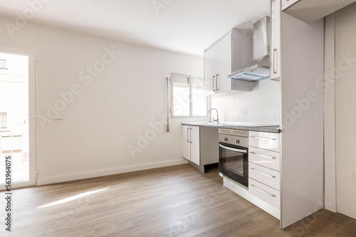 White wooden furniture recently installed in the absence of some appliances in an empty room with access to a terrace