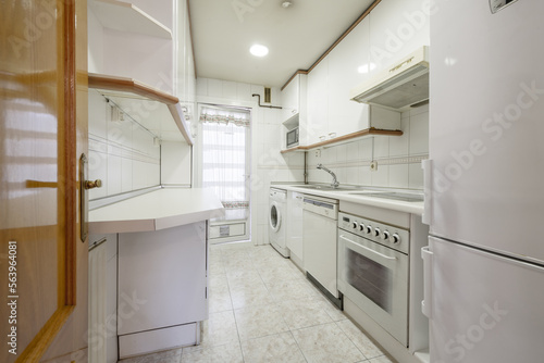 Narrow kitchen with white cabinets with countertop of the same color and built-in appliances of the same color