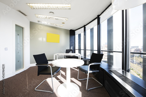 Office with a small white round table next to a large window with a view, curved walls and a technical ceiling