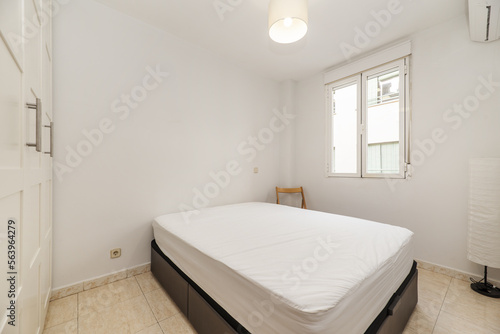 Bedroom with a double bed and a three-section white wardrobe, an aluminum window and a lamp in one corner