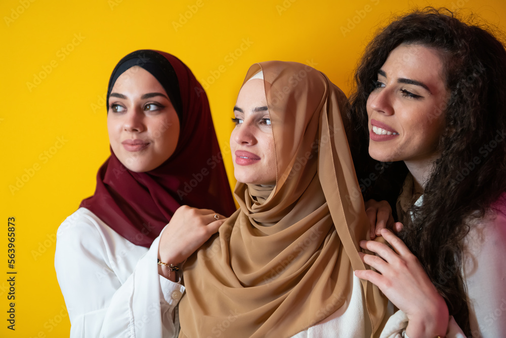 Group portrait of beautiful Muslim women two of them in a fashionable dress with hijab isolated on a yellow background Group portrait of beautiful Muslim women two of them in a fashionable dress with hijab isolated on a yellow background