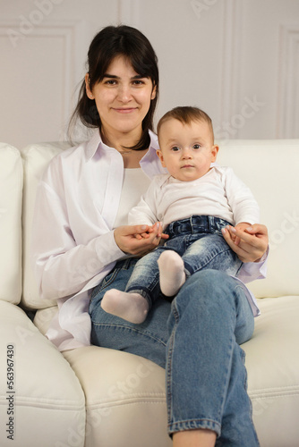 Portrait of a young loving mother with a small child in his arms sitting on the sofa