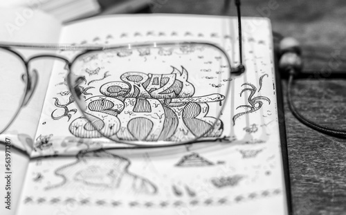 Artist sketchbook with nankin ink doodle drawings over a wooden textured table. A leather pencil case is full of drawing materials.