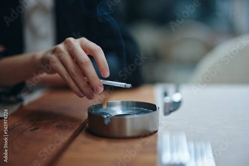 A woman with a cigarette in her hands shakes the ashes into an ashtray, close-up