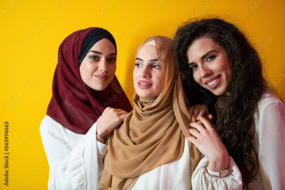 Group portrait of beautiful Muslim women two of them in a fashionable dress with hijab isolated on a yellow background Group portrait of beautiful Muslim women two of them in a fashionable dress with hijab isolated on a yellow background