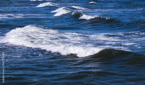Shore waves with white foam goes over deep blue water © evannovostro