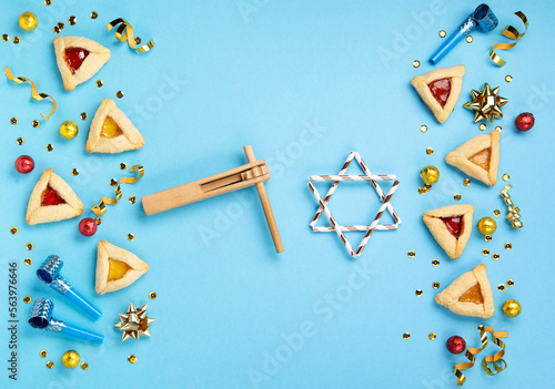 Purim celebration jewish carnival holiday concept. Tasty hamantaschen cookies, Carnival mask, noisemaker, sweet candies and party decor on blue background. Top view, flat lay, copy space.