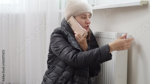 Young woman feeling cold at home calling repairmain to fix broken heating radiator. Concept of energy crisis, high bills, broken heating system, economy and saving money on monthly utility payments.