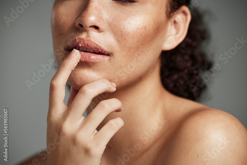 Woman, hand and lips in sugar scrub for skincare, makeup or cosmetics against a grey studio background. Happy female applying treatment for facial cosmetic, lip dermatology or mouth exfoliation photo