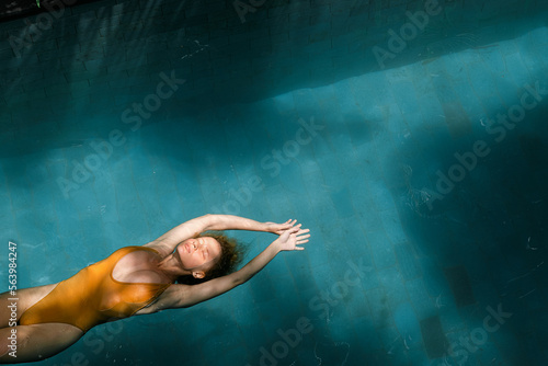 A beautiful girl in a yellow swimsuit swims on her back in the pool  top view.