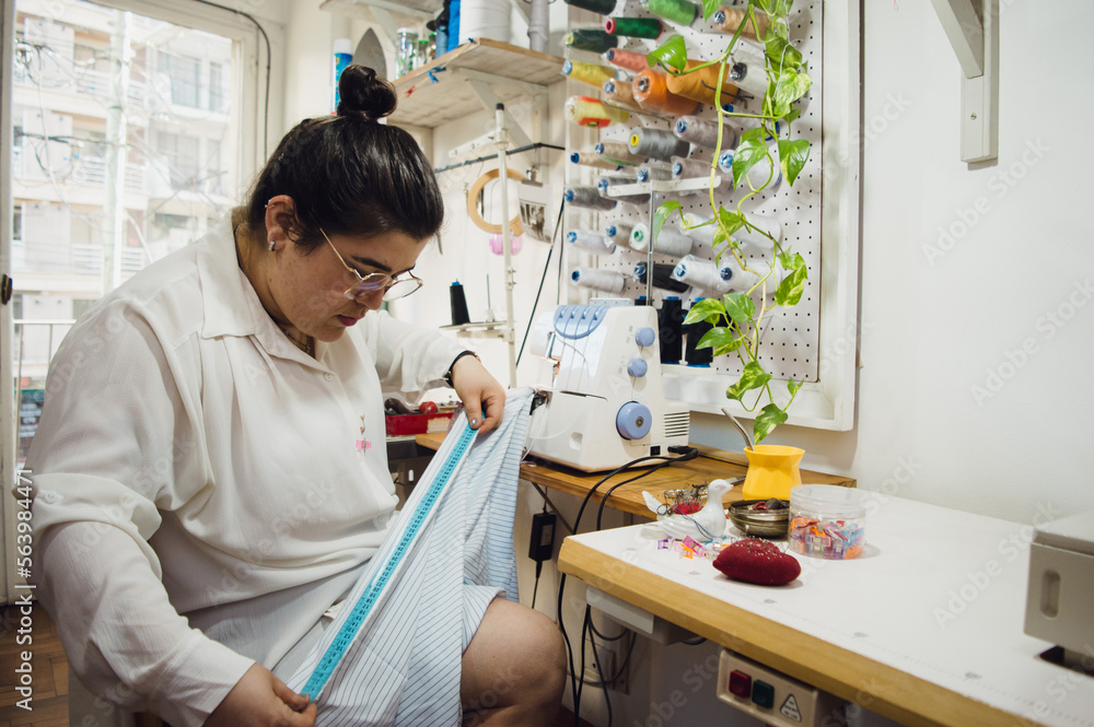 young woman seamstress sitting working measuring fabric with a tape measure young woman seamstress sitting working measuring fabric with a tape measure