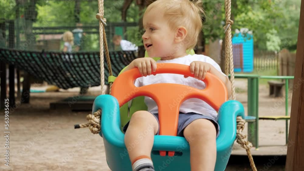 Slow motion of happy smiling baby boy having fun swinging in colorful swing at park. Kids playing outdoors, children having fun, summer vacation and holiday Slow motion of happy smiling baby boy having fun swinging in colorful swing at park. Kids playing outdoors, children having fun, summer vacation and holiday