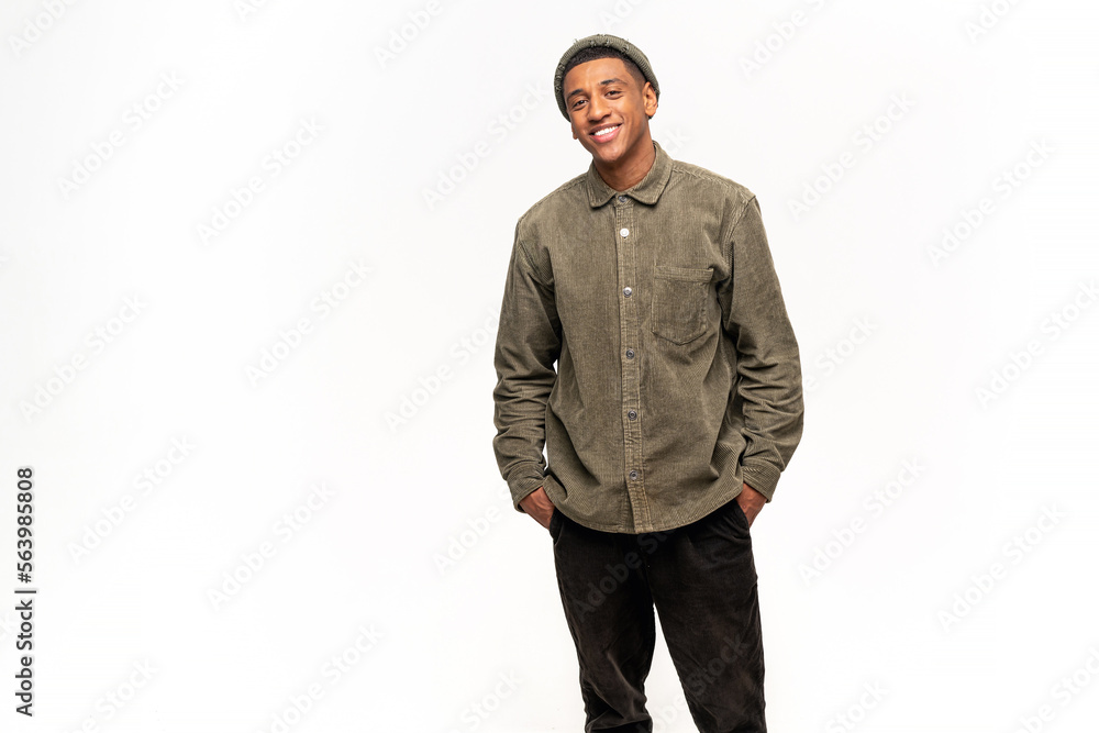 Portrait of happy satisfied handsome young man in shirt standing with arms at the pockets and looking at camera with toothy smile. Indoor studio shot on white background