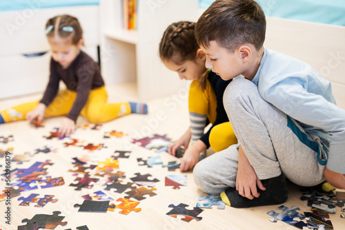 Children connecting jigsaw puzzle pieces in a kids room on floor at home. Fun family activity leisure.