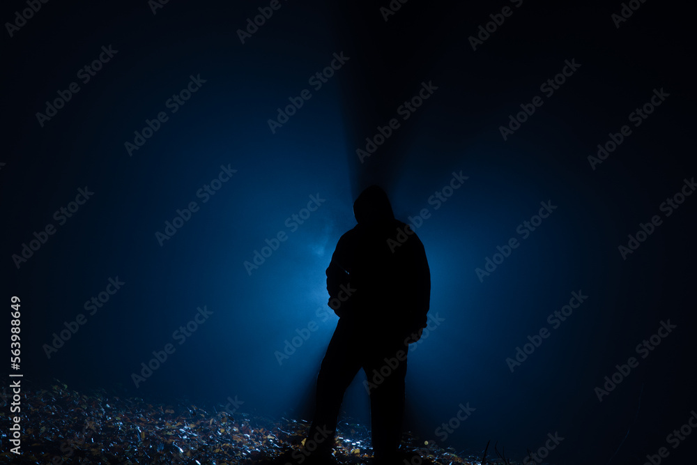 Hooded man in the dark forest at backlight Hooded man in the dark forest at backlight