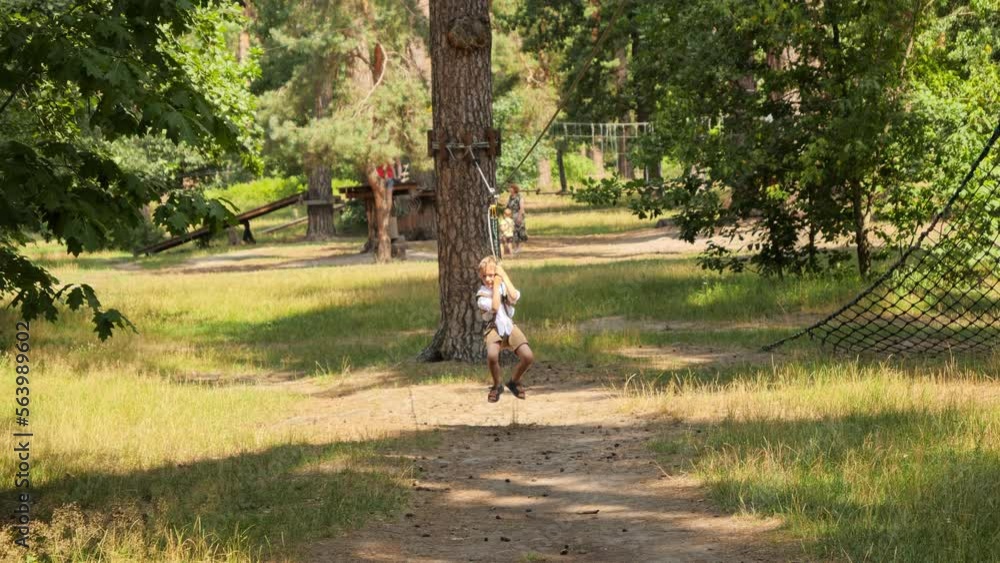 Happy laughing boy having fun riding on the zip line at summer park. Active childhood, healthy lifestyle, kids playing outdoors, children in nature Happy laughing boy having fun riding on the zip line at summer park. Active childhood, healthy lifestyle, kids playing outdoors, children in nature