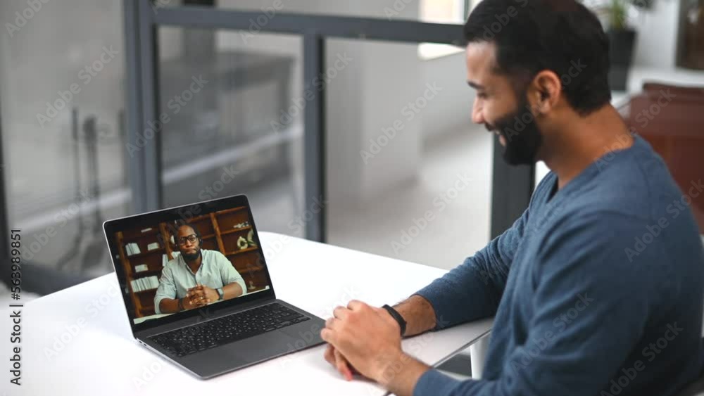 Two diverse male colleagues taking part in video meeting. Multiracial business partners involved virtual conference. Back view male Indian student takes an online language classes from African teacher Two diverse male colleagues taking part in video meeting. Multiracial business partners involved virtual conference. Back view male Indian student takes an online language classes from African teacher