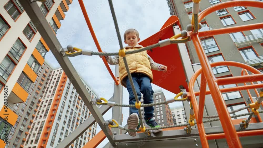 custom made wallpaper toronto digitalView from the ground on little boy walking over the rope bridge at playground. Active child, sports and development, kids playing outdoors.