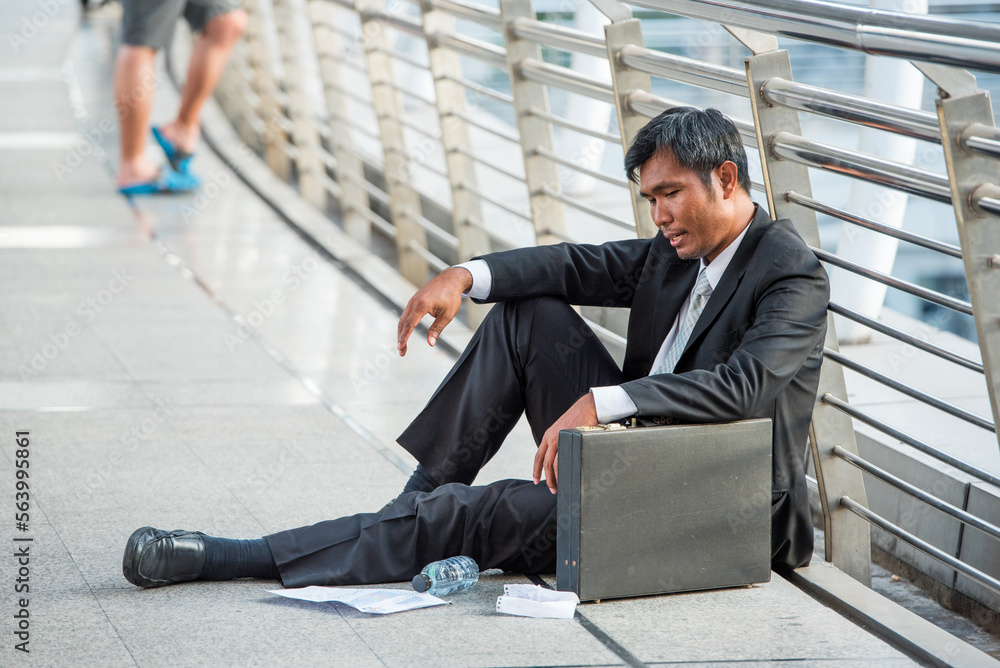 Fototapeta premium businessman in suit fired from job sitting sad outside office in city background Unemployment, unemployed man with leather briefcase sit on street he loss job.