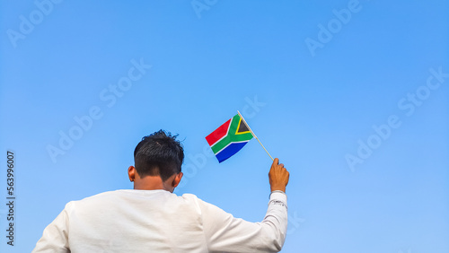 Boy holding South Africa flag against clear blue sky. Man hand waving South African flag view from back, copy space