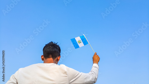 Boy holding Guatemala flag against clear blue sky. Man hand waving Guatemalan flag view from back, copy space