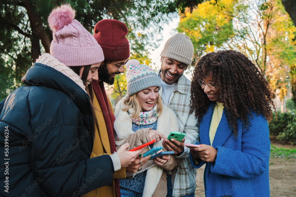 Portrait of a group of multiracial young fiends watching videos on a social media app using an cellphone with autumn clothes. Multiethnic people having fun using their smartphones. Communication