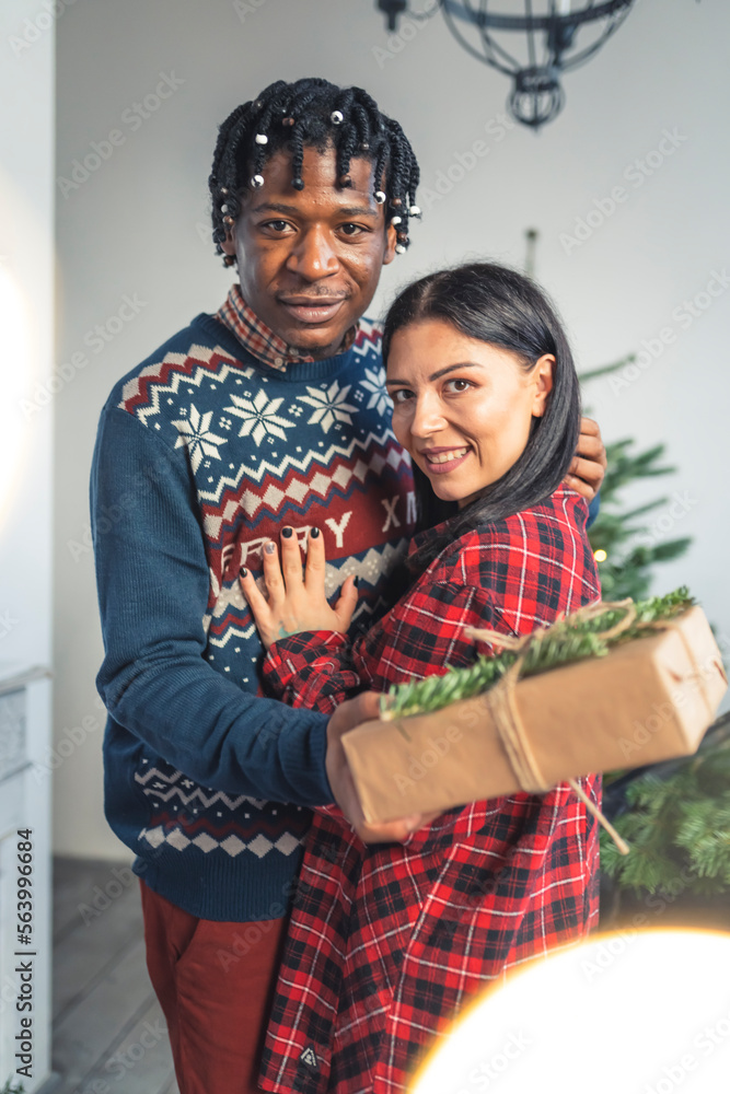 Interacial couple standing together with presents near the Christmas tree. High quality photo Interacial couple standing together with presents near the Christmas tree. High quality photo